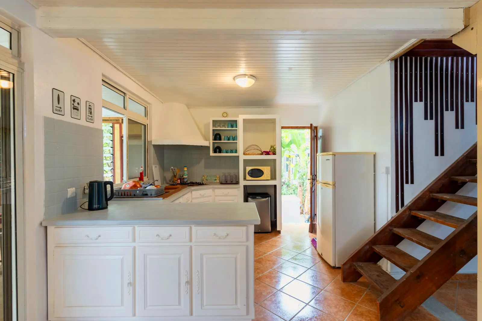 Cuisine partagée : plan de travail blanc, gazinière, micro-ondes, frigo et escalier en bois